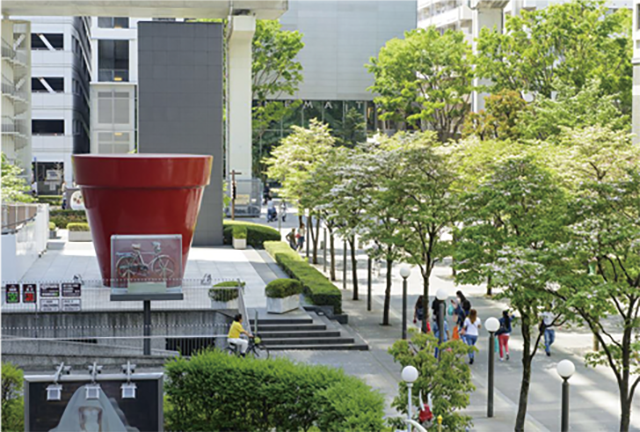 ファーレ立川の街区風景。イタリア語の「FARE（創る・創造する・生み出す）」に立川の頭文字「T」を付けた街区「ファーレ（FARET）立川」には世界36カ国92人の作家による109点のパブリックアート「ファーレ立川アート」が点在する。写真は作品番号070の「オープンカフェテラス」（ジャン＝ピエール・レイノー作）と名付けられた赤い植木鉢と自然石で構成された作品